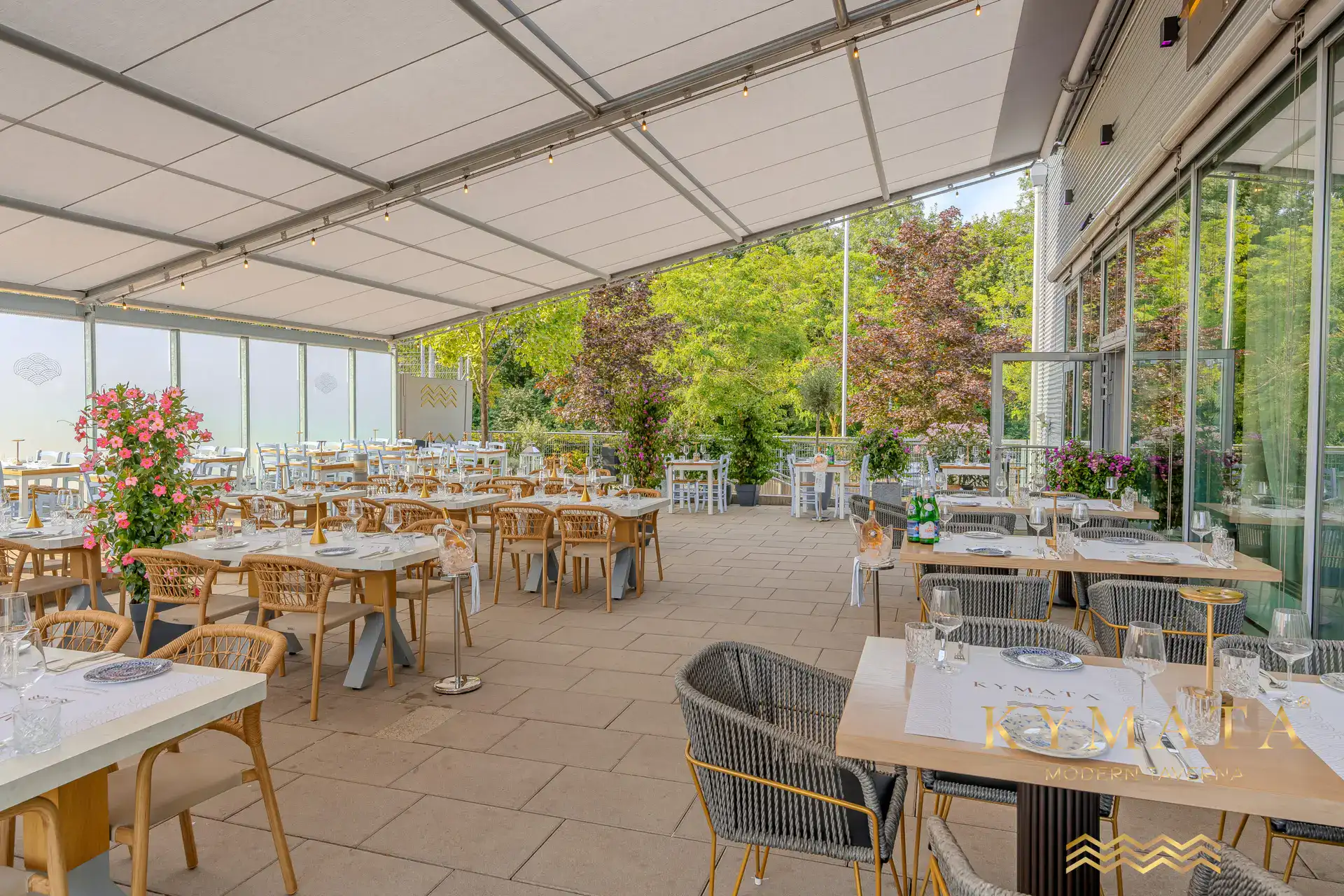 Gedeckte Tische und viel Grün auf der Terrasse des Kymata unter der Pergola