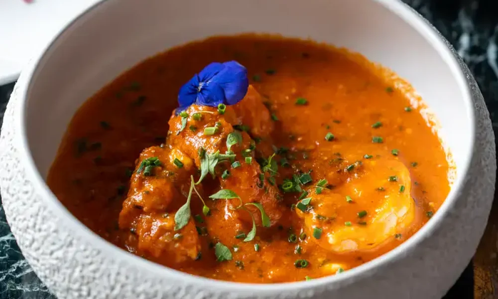 Geschmackvolles indisches curry mit fleisch und ei, garnierte mit frischen kräutern und blüten auf schwarzem marmor tisch.