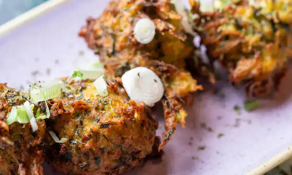 Knusprige vegetarische Frikadellen auf einem stilvollen, modernen Teller mit frischen Zwiebeln und Kräutern, Präsentation in zeitgemäßem Design, kulinarisch im Trend, innovative Küche, hochwertige Zutaten.