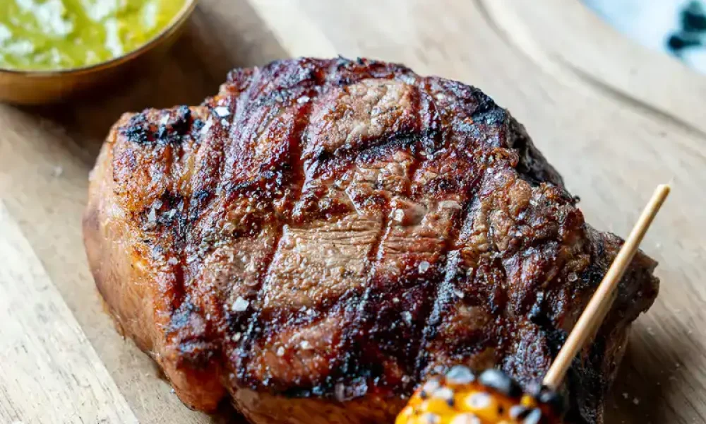 Gegrilltes Steak mit Maiskolben und Chilisauce auf Holzplatte, modernes Grillgericht, saftiges Fleisch, BBQ Spezialität, kulinarische Genussmomente, hochwertiges Grillfleisch, summer barbecue, Kymata Modern.